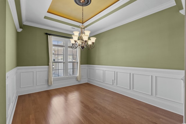empty room featuring wainscoting, a tray ceiling, a notable chandelier, and crown molding