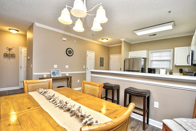 dining room featuring wood finished floors, a chandelier, ornamental molding, a textured ceiling, and electric panel