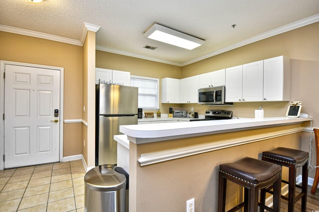 kitchen featuring appliances with stainless steel finishes, a peninsula, white cabinetry, a kitchen breakfast bar, and light countertops