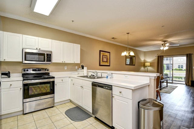 kitchen featuring appliances with stainless steel finishes, a peninsula, light countertops, a sink, and crown molding