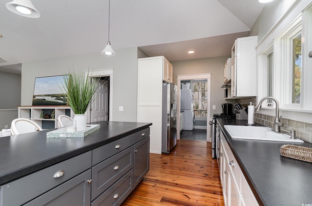 kitchen featuring a sink, tasteful backsplash, wood finished floors, stainless steel appliances, and dark countertops