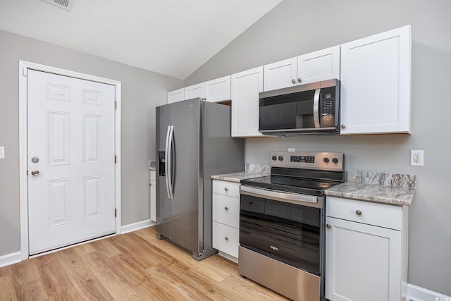 kitchen featuring appliances with stainless steel finishes, light wood finished floors, white cabinetry, baseboards, and lofted ceiling