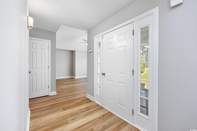 foyer entrance featuring baseboards, ceiling fan, light wood finished floors, and a textured ceiling