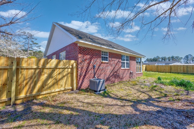 view of side of property with a fenced backyard, a lawn, central AC, and brick siding