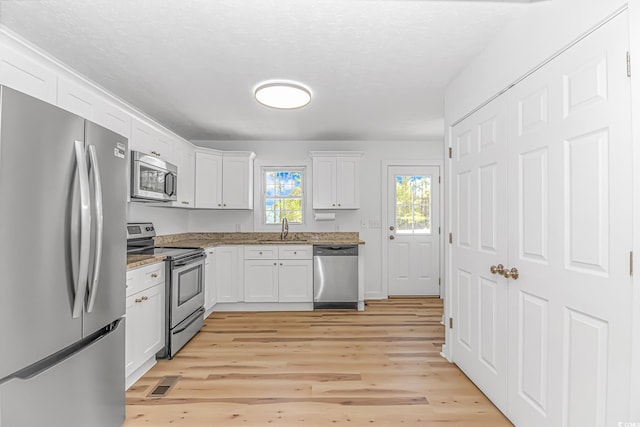 kitchen with a sink, light wood-style floors, white cabinetry, stainless steel appliances, and light stone counters