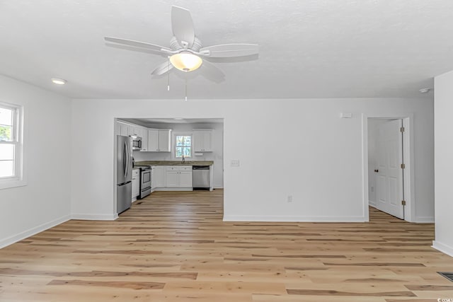 unfurnished living room with light wood finished floors, baseboards, a ceiling fan, and plenty of natural light