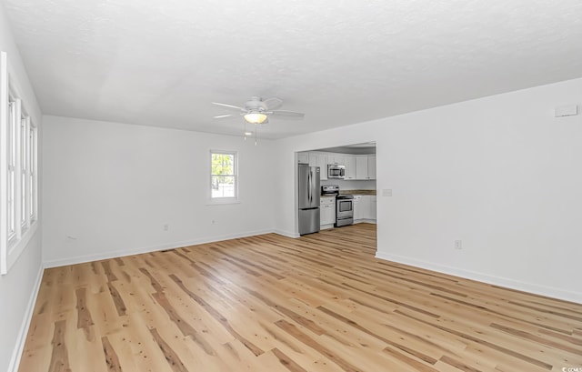unfurnished living room with baseboards, a ceiling fan, light wood-style floors, and a textured ceiling