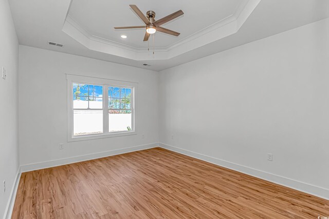 unfurnished room with visible vents, a raised ceiling, ornamental molding, ceiling fan, and light wood-style floors