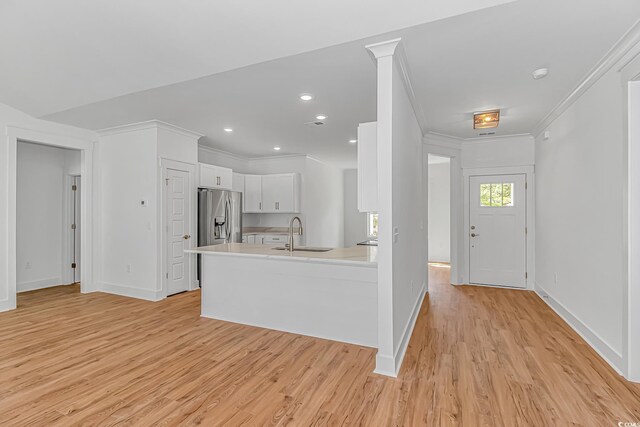 kitchen featuring stainless steel fridge with ice dispenser, light wood-type flooring, white cabinets, a sink, and light countertops
