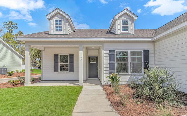 doorway to property with covered porch, a lawn, and roof with shingles