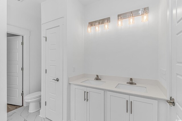 bathroom featuring double vanity, marble finish floor, a sink, and toilet