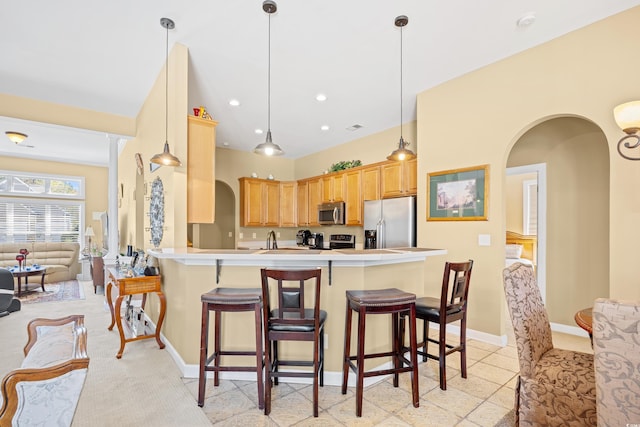 kitchen with arched walkways, a peninsula, a kitchen breakfast bar, and appliances with stainless steel finishes
