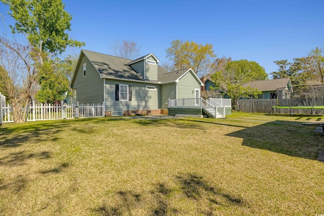 back of house featuring a yard, a wooden deck, a trampoline, and a fenced backyard
