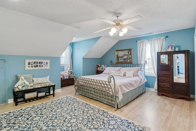 bedroom with a textured ceiling, wood finished floors, vaulted ceiling, and multiple windows
