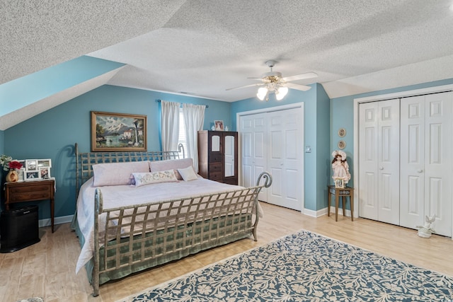 bedroom featuring lofted ceiling, wood finished floors, two closets, and baseboards