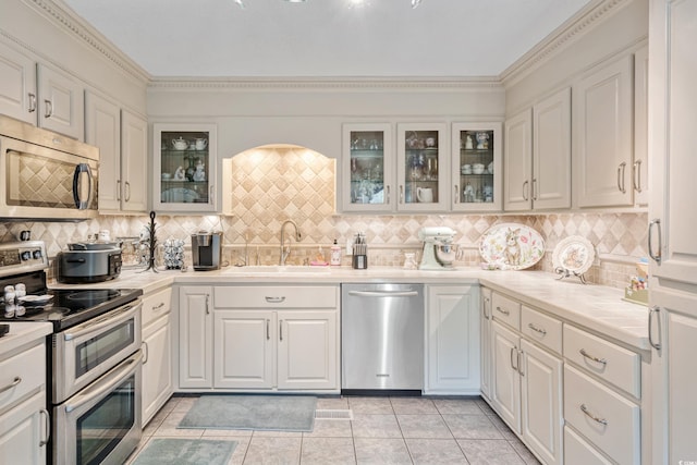 kitchen with a sink, decorative backsplash, light tile patterned floors, white cabinetry, and appliances with stainless steel finishes