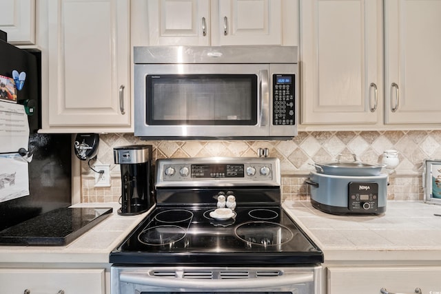 kitchen with appliances with stainless steel finishes, tile counters, and backsplash
