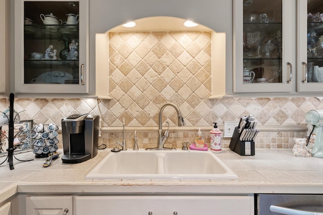 kitchen featuring white cabinets, backsplash, glass insert cabinets, and a sink