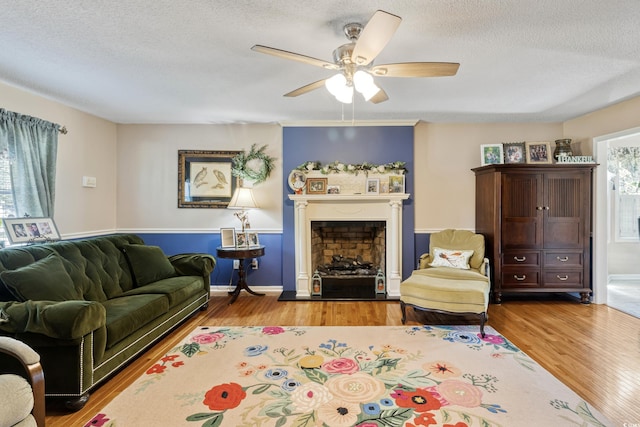 living area with wood finished floors, ceiling fan, a textured ceiling, and a fireplace