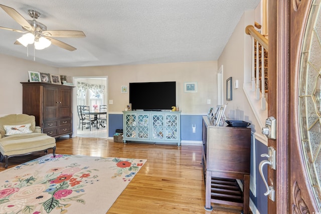 living area with a textured ceiling, wood finished floors, a ceiling fan, and stairs