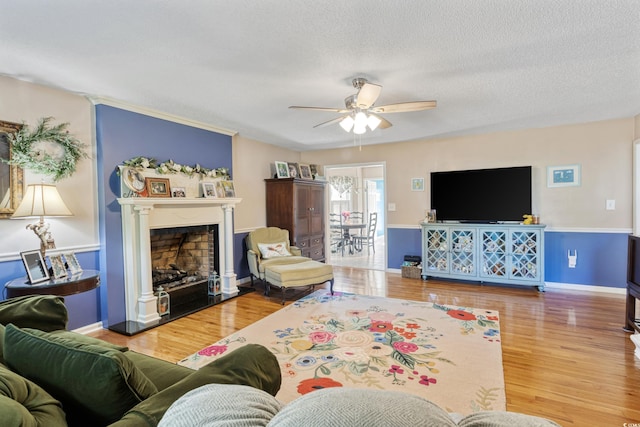 living area featuring wood finished floors, ceiling fan, a textured ceiling, and a fireplace with raised hearth