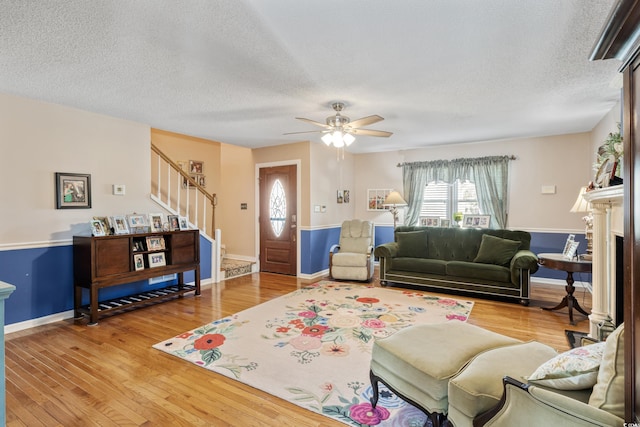 living room with stairway, ceiling fan, light wood finished floors, and a textured ceiling
