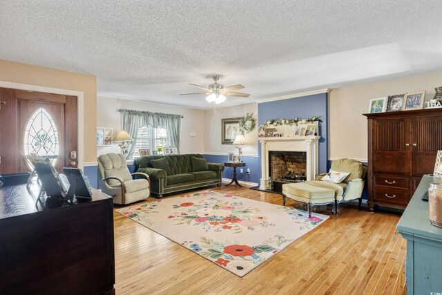 living area featuring light wood-type flooring, ceiling fan, a textured ceiling, and a fireplace with raised hearth