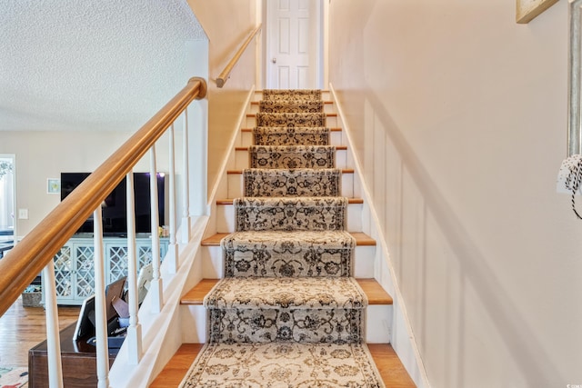 stairs with a textured ceiling and wood finished floors