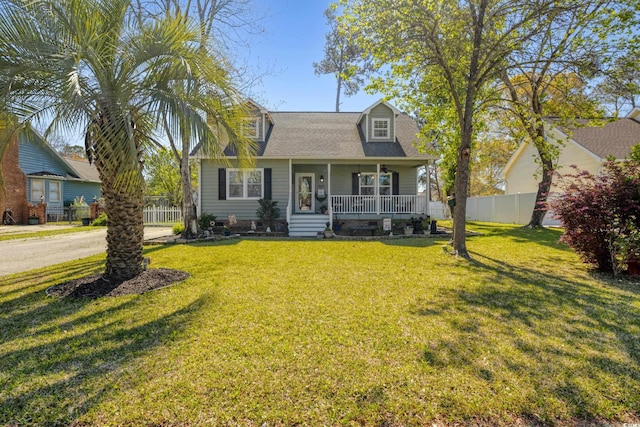 cape cod house with a front yard, roof with shingles, covered porch, and fence