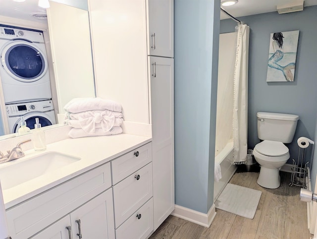 bathroom featuring toilet, stacked washer and dryer, wood finished floors, and vanity
