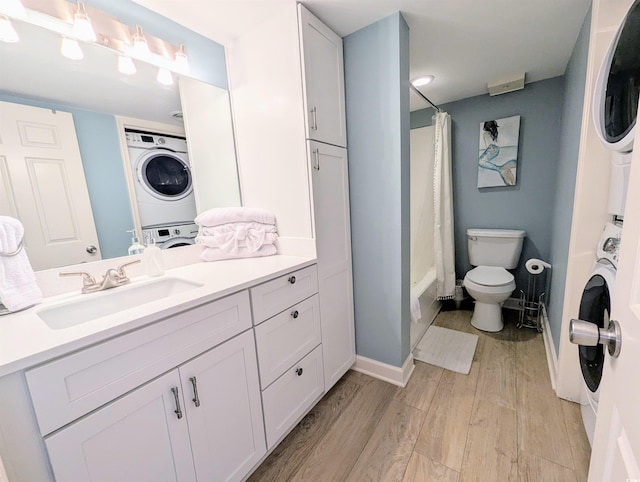 full bath with toilet, wood finished floors, vanity, and stacked washer / drying machine