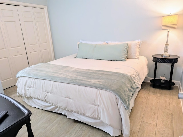 bedroom with a closet, light wood finished floors, and baseboards