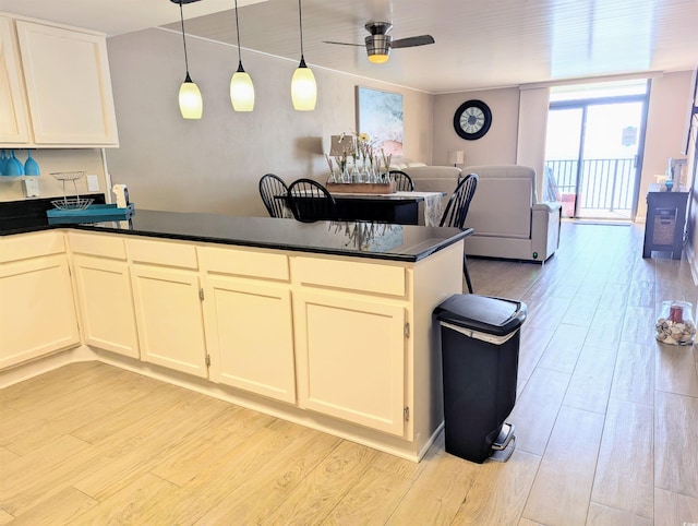 kitchen with dark countertops, a peninsula, a ceiling fan, and light wood finished floors
