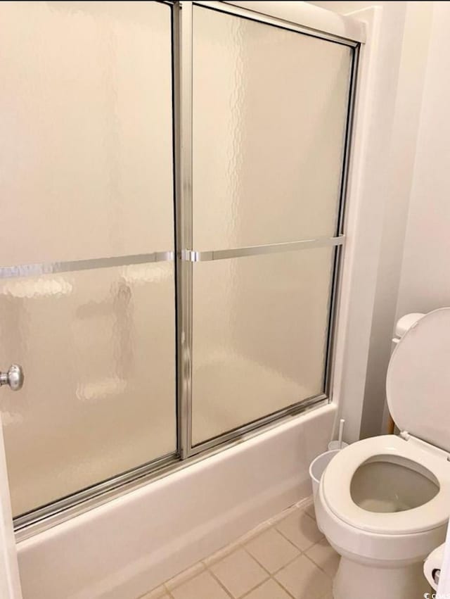 full bath with tile patterned flooring, toilet, and bath / shower combo with glass door