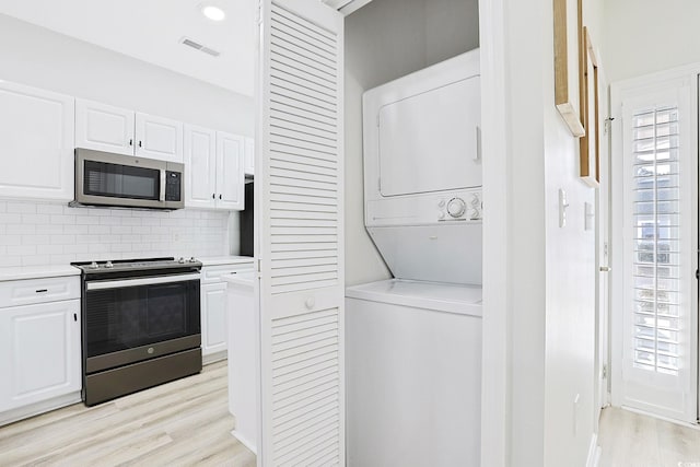 clothes washing area with stacked washer / drying machine, visible vents, laundry area, and light wood-style floors