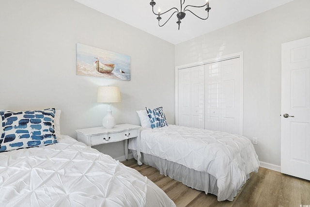 bedroom featuring an inviting chandelier, baseboards, a closet, and wood finished floors
