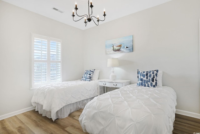 bedroom with baseboards, wood finished floors, a chandelier, and visible vents