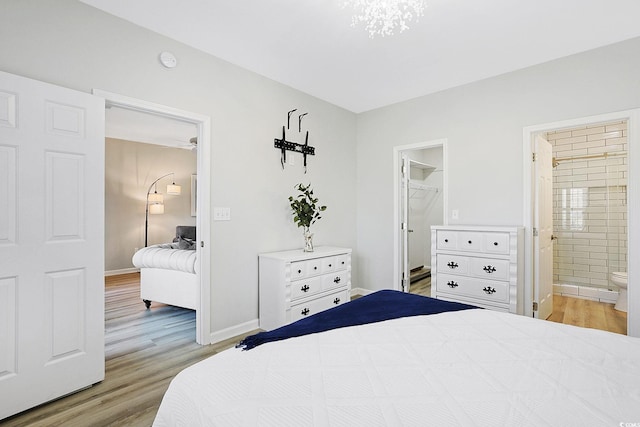 bedroom featuring a walk in closet, ensuite bathroom, baseboards, and wood finished floors