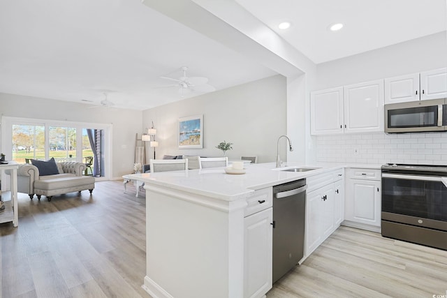 kitchen with appliances with stainless steel finishes, a sink, a peninsula, open floor plan, and backsplash