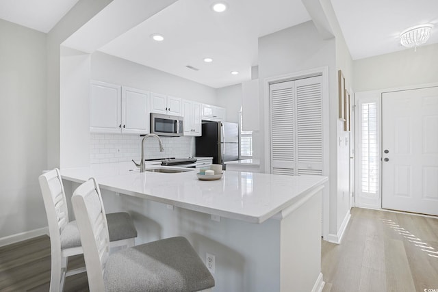 kitchen featuring a peninsula, baseboards, light wood-type flooring, tasteful backsplash, and stainless steel appliances
