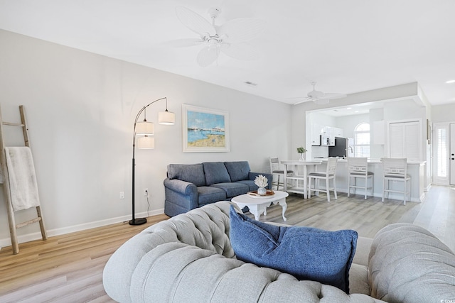 living room with baseboards, a ceiling fan, and light wood finished floors