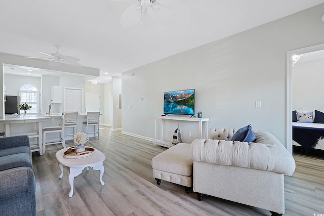 living room with a ceiling fan, baseboards, and light wood-style flooring