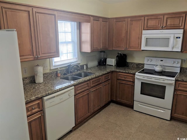 kitchen featuring white appliances, a sink, and dark stone countertops
