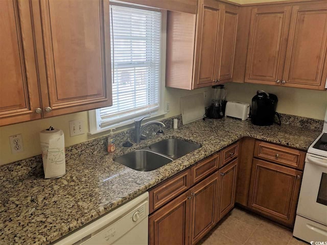 kitchen with brown cabinetry, white appliances, light stone counters, a sink, and light tile patterned floors