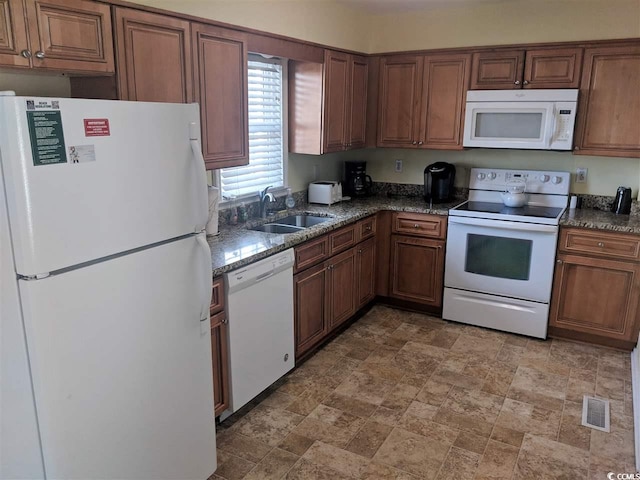 kitchen featuring brown cabinetry, stone finish flooring, visible vents, a sink, and white appliances