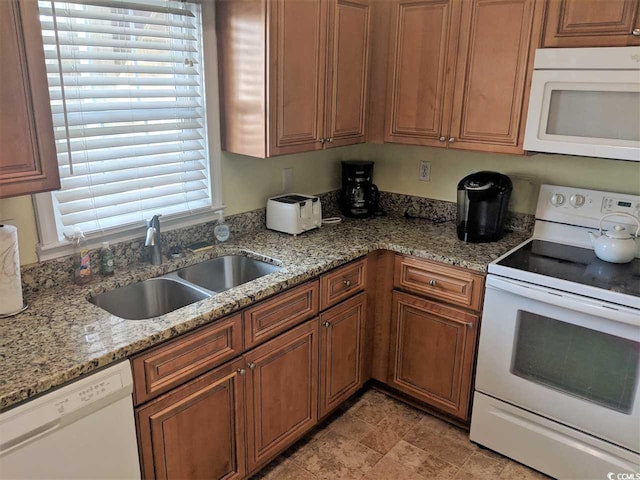 kitchen with a sink, brown cabinetry, white appliances, and light stone countertops