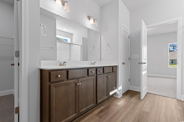 full bathroom featuring a shower, wood finished floors, a sink, double vanity, and baseboards