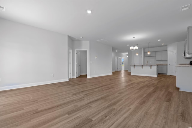 unfurnished living room with visible vents, baseboards, a chandelier, recessed lighting, and light wood-style flooring