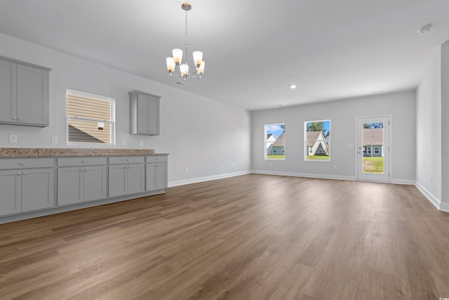 unfurnished living room featuring baseboards, a chandelier, and wood finished floors