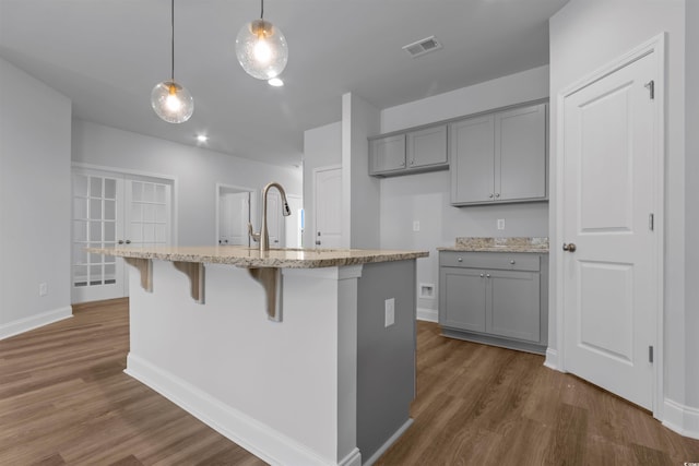 kitchen with dark wood-style floors, gray cabinetry, light stone countertops, visible vents, and pendant lighting